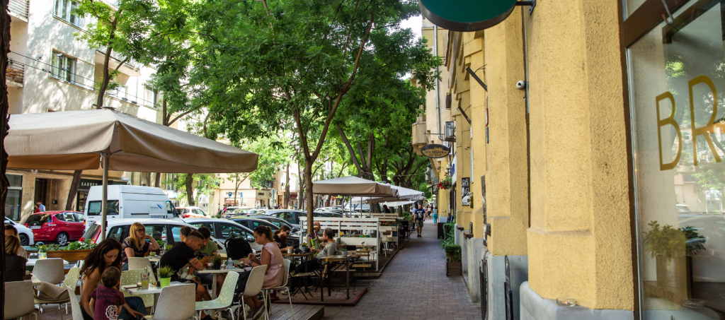 Street cafés on Pozsonyi Street in Budapest, where locals enjoy breakfast under leafy trees.