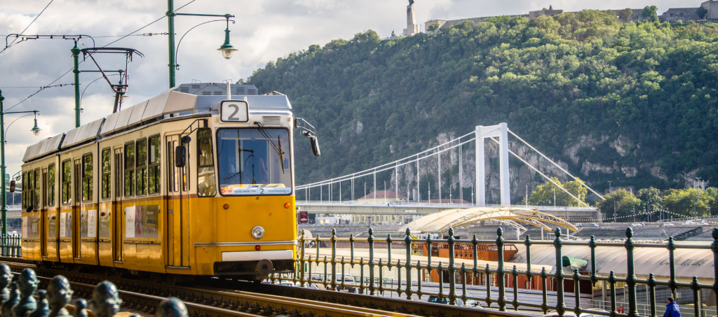 Budapest’s iconic #2 tram passing along the Danube with a view of Gellért Hill.