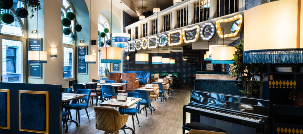 Cozy interior of VakVarjú Budapest with elegant blue décor, warm lighting, and a piano in the dining area.