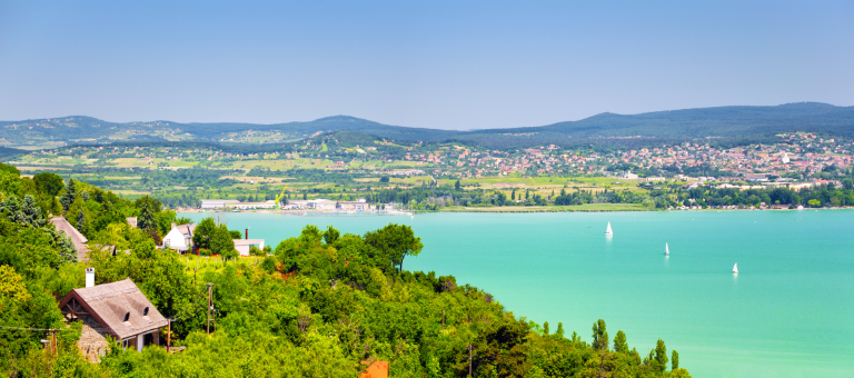 Panoramic view of Lake Balaton with turquoise water, sailboats, and vineyards on the hills of the north shore in Hungary.