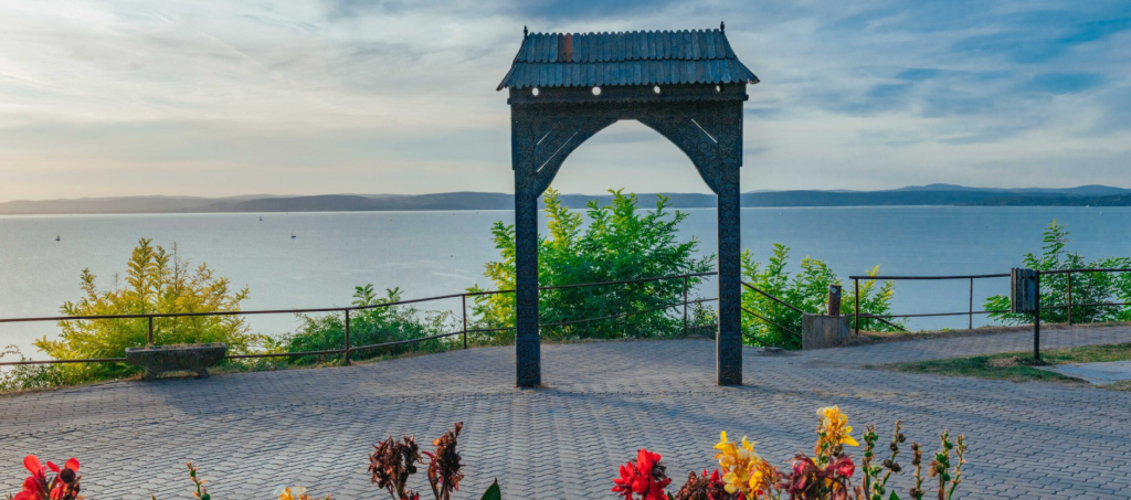 Scenic viewpoint at Lake Balaton with a traditional carved wooden gate and colorful flowers in the foreground