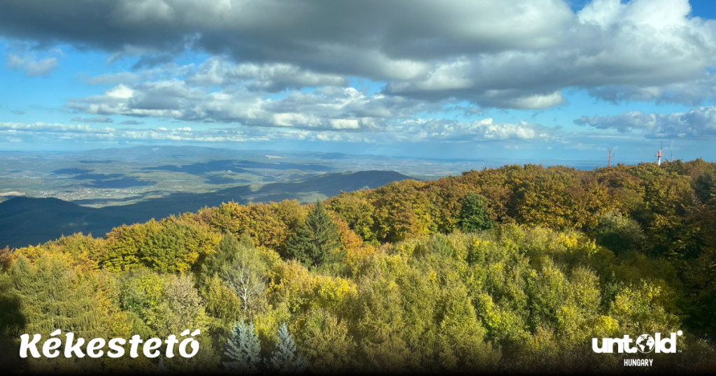 Scenic autumn view from Kékestető, the highest mountain in Hungary, with colorful forest and distant hills under a blue sky.