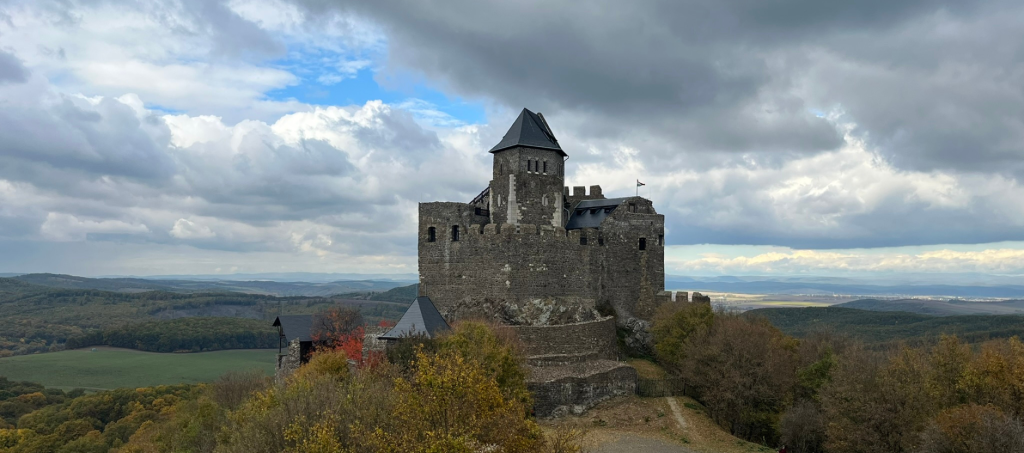 Stone ruins of Hollókő Castle above the UNESCO-listed village, surrounded by rolling hills and traditional houses.