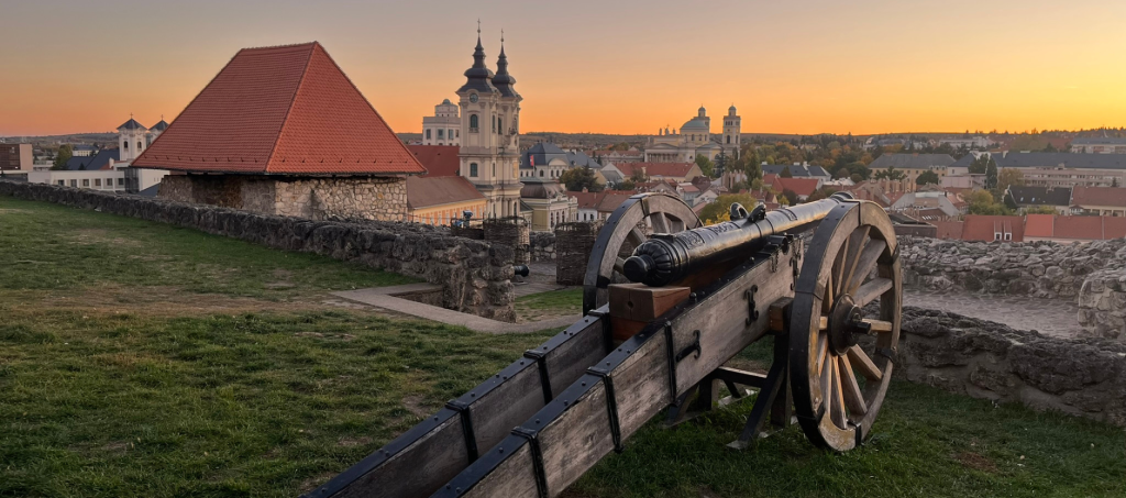 Sunset over Eger Castle with historic cannons overlooking the city’s baroque skyline and the iconic cathedral in the distance.