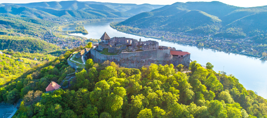 Panoramic aerial view of Visegrád Castle overlooking the Danube Bend, surrounded by lush green hills and riverside villages.