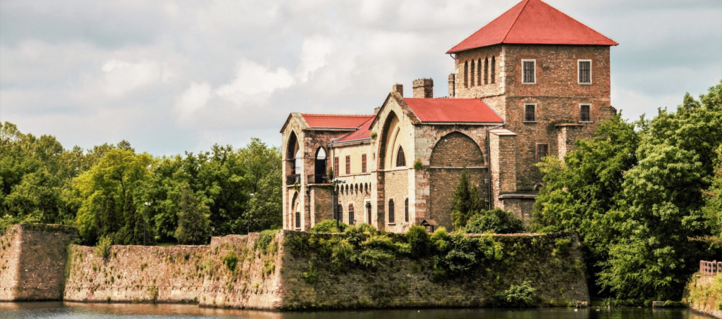Reflection of Tata Castle in the calm waters of Öreg-tó with the Renaissance-style fortress framed by trees.