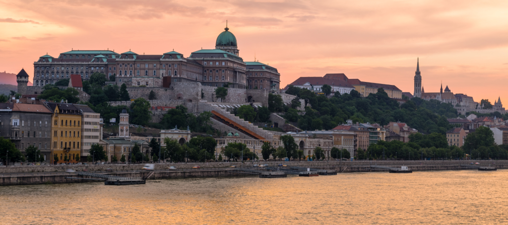 Panoramic sunset view of Buda Castle and the Danube River, showcasing the grand palace and historic Castle District.